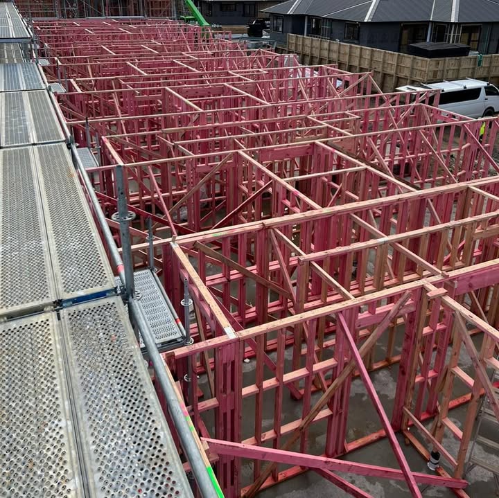 Rows of pink timber-framed multi-unit blocks side-by-side with metal scaffold platforms