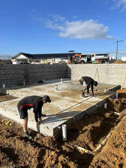 Two LTK workers screeding a fresh concrete pad inside completed boundary block walls